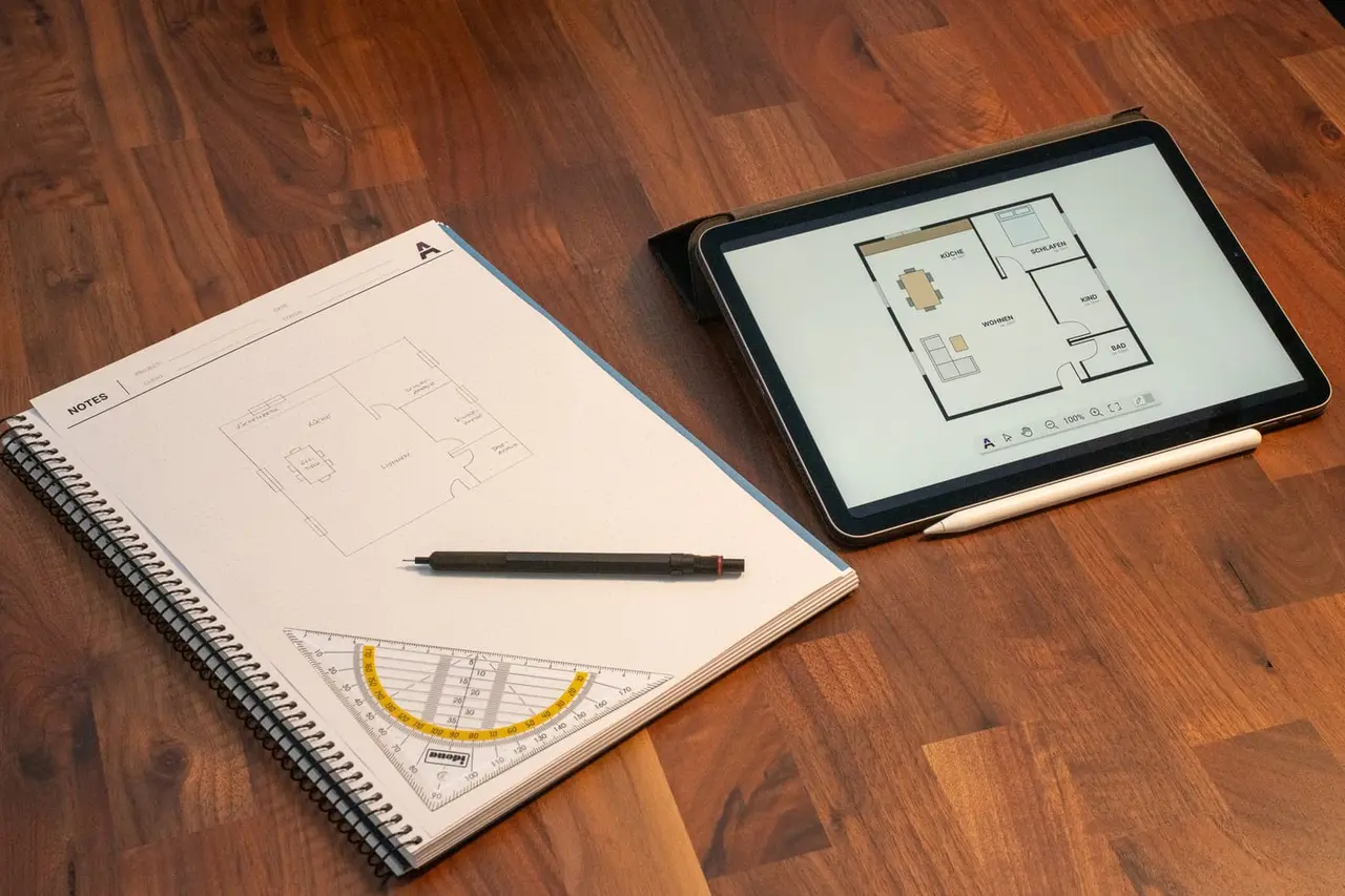 A notebook with a hand-drawn floor plan sits next to a tablet showing the same plan as an interactive SVG rendering.