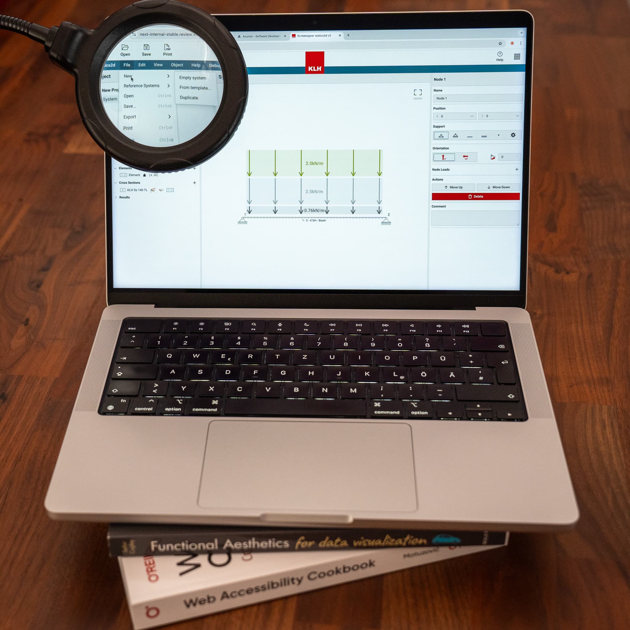 Image of a laptop on a stack of accessibility books. On it, there is a screen with a floor illustration. A magnifying glass zooms in on a menu bar.